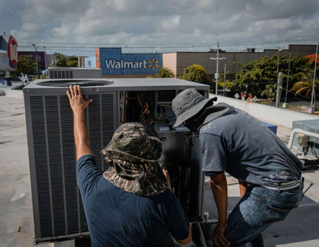 Two technicians repair a rooftop HVAC unit outside a Walmart store.